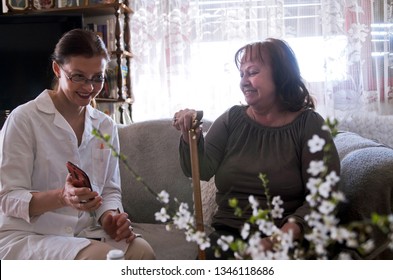 Young Female Nurse And Elderly Woman Watching Fun Photos On Smart Phone And Smile.Care For Old People At Home.Smiling Is Healthy