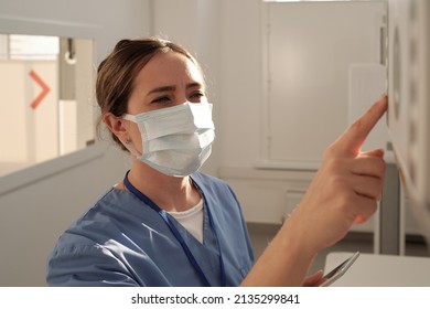 Young Female Nurse Or Radiologist In Uniform And Protective Mask Pushing Button On Panel Of X-ray Machine During Work In Clinics