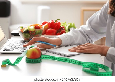 Young female nutritionist working with laptop and notebook at table in office, closeup - Powered by Shutterstock