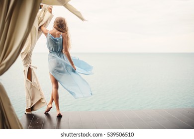 Young Female On Beach Terrace Wearing Blue Dress. Beautiful Summer Woman On The Beach