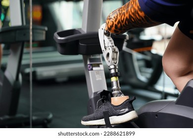 Young female with one prosthetic leg with exercising with a spinning bike in the gym to practice joint use with the other normal leg to be flexible, Concept of living a woman's life with a prosthetic - Powered by Shutterstock