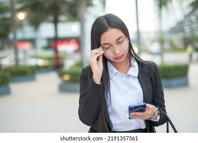 A Young Female Paralegal Is Strolling Outside The Park While Checking Her Cellphone For Messages During Her Break Time. A Paralegal Is Reading A Legal Case Via Email While Heading To Her Office.