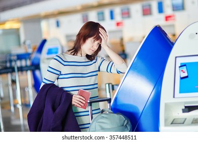 Young female passenger at the airport, doing self check-in, stressed and concerned. Missed, delayed or canceled flight concept