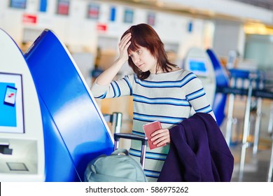 Young female passenger at the airport, doing self check-in, stressed and concerned. Missed, delayed or cancelled flight concept
