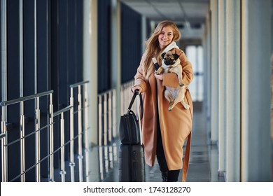 Young female passenger in warm clothes walking with her dog in airport hall.