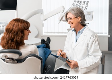 A young female patient is sitting in the dentist's chair, engaging in conversation and sharing smiles with the dentist. Consultation is taking place in the dentist's office. - Powered by Shutterstock