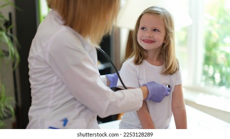 Young female patient smiles at doctor at medical examination. Nurse listens to heartbeat of happy girl in medical clinic. - Shutterstock ID 2253128289