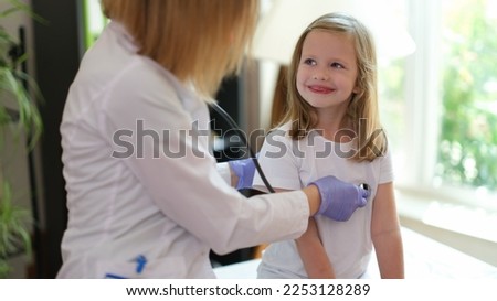 Young female patient smiles at doctor at medical examination. Nurse listens to heartbeat of happy girl in medical clinic.