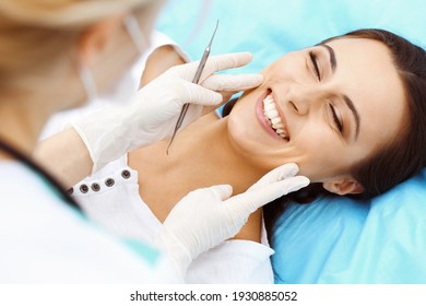 Young Female Patient Visiting Dentist Office.Beautiful Woman With Healthy Straight White Teeth Sitting At Dental Chair With Open Mouth During Oral Checkup While Doctor Working At Teeth