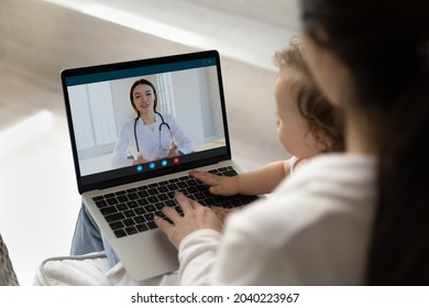 Young female pediatrician giving consultation to new mom from laptop screen. Young mother holding toddler baby in arms, making video call, consulting doctor. Infant healthcare, childcare concept