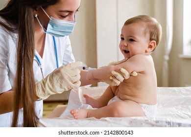 Young Female Pediatrician Or Nurse Giving An Intramuscular Injection Of A Vaccine To Hand Of Little Baby Boy Immunization For Children Concept. Happy Little Cute Boy Getting A Flu Shot Not Afraid Of