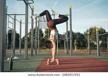 Young female performs an advanced pose on parallettes at a park, showcasing flexibility and strength