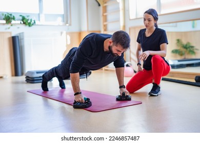 Young female personal trainer with red leggings training a young man with beard in an indoor training centre - Powered by Shutterstock