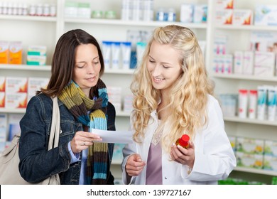 Young Female Pharmacist And Customer Reading Prescription Paper At Pharmacy Counter