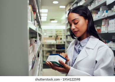 Young Female Pharmacist Reading Instructions On Medicine Box Standing In Aisle Of Chemist