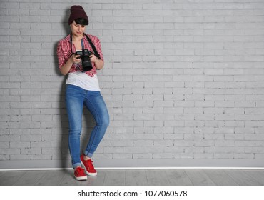 Young female photographer with camera near brick wall