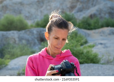 Young Female Photographer Checking Her Camera Settings Before A Photoshoot Outside In An Abandoned Quarry.