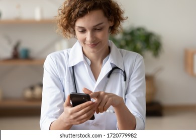 Young Female Physician Using Mobile Healthcare Tech App Consulting Remote Patient Online In Telemedicine Software. Woman Doctor Therapist Holding Smart Phone Texting Message For Digital Consultation.