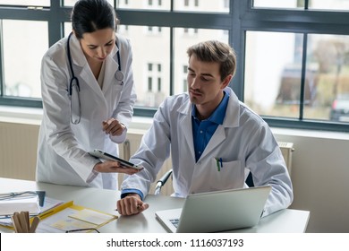 Young female physician using a tablet PC while asking for advice from her experienced male colleague in the office a modern hospital - Powered by Shutterstock