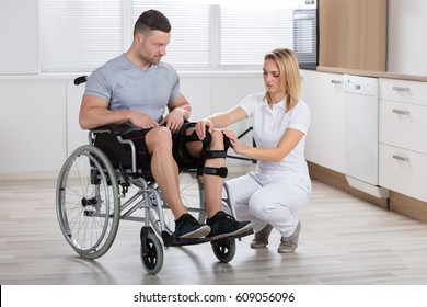 Young Female Physiotherapist Fixing Knee Braces On Man's Leg In A Clinic