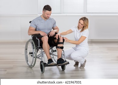 Young Female Physiotherapist Fixing Knee Braces On Man's Leg In A Clinic