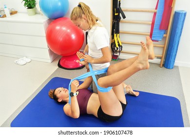 Young Female Physiotherapist Working With Her Patient, Exercising With Rubber Bands Around Legs And Arms