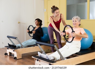 Young female pilates instructor assisting elderly woman to do exercises on reformer with flex ring and fitball. Active lifestyle concept - Powered by Shutterstock