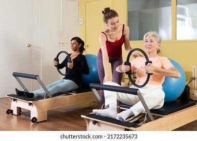 Young female pilates instructor assisting elderly woman to do exercises on reformer with flex ring and fitball. Active lifestyle concept - Powered by Shutterstock