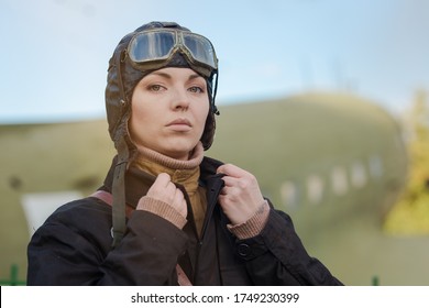 A Young Female Pilot In Uniform Of Soviet Army Pilots During The World War II. Black Flying Jumpsuit, Helmet And Goggles. Photo In Retro Style.