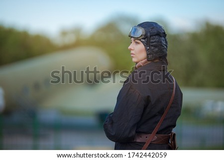 A young female pilot in uniform of Soviet Army pilots during the World War II. Black flying jumpsuit, helmet and goggles. Photo in retro style.