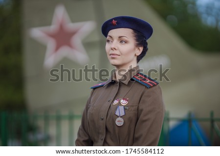 A young female pilot in uniform of Soviet Army pilots during the World War II. Military shirt with shoulder straps of a major and a beret. Against the background of a military aircraft.