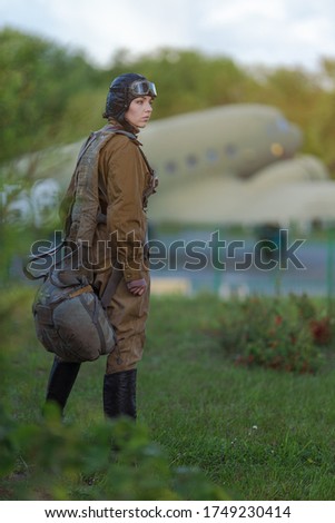 A young female pilot in uniform of Soviet Army pilots during the World War II. Military shirt with shoulder straps of a major, parachute, flight helmet and goggles.