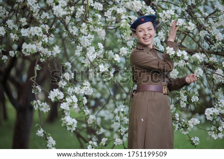 A young female pilot in uniform of Soviet Army pilots during the World War II. Military shirt with shoulder straps of a major and a beret. In spring blooming apple orchard