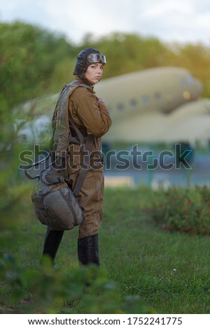 A young female pilot in uniform of Soviet Army pilots during the World War II. Military shirt with shoulder straps of a major, parachute, flight helmet and goggles.