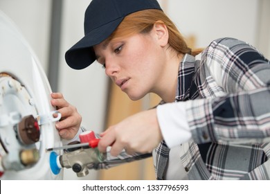 Young Female Plumber Working On Water Heater