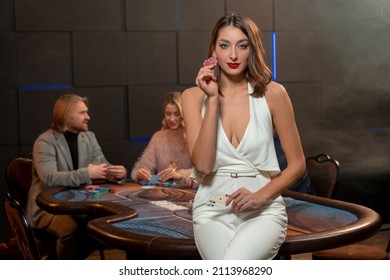 Young Female Poker Player Sitting On Gaming Table With Cards And Betting Chips