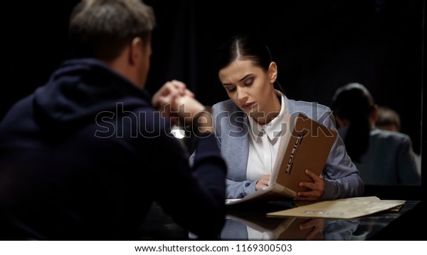 Young female police officer comparing suspect\
statements with file\
documents