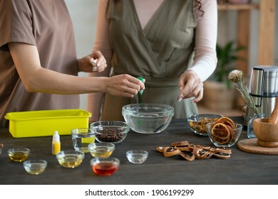 Young Female Pouring Liquid Green Colorant Into Bowl With Melted Soap Mass While Another Woman Mixing It Before Making Cosmetic Products