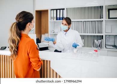 Young Female Practitioner Or Nurse With Face Protective Mask Working At Clinic Reception Desk. She Is Helping To Patient To Make Contactless Payment For Medical Services.