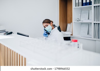 Young Female Practitioner Or Nurse With Face Protective Mask Working At Clinic Reception Desk. 