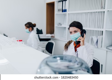 Young Female Practitioner Or Nurse With Face Protective Mask Working At Clinic Reception Desk. 