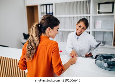 Young Female Practitioner Or Nurse Working At Clinic Reception Desk.	