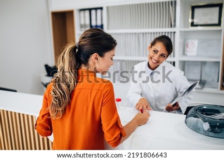 Young female practitioner or nurse working at clinic reception desk.	