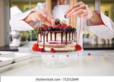 Young Female Professional Baker Decorating A Chocolate And Cream Naked Cake With Blueberries