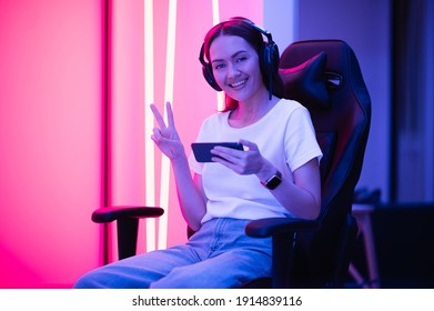 Young Female Professional Cybersport Gamer Play Mobile Game By Smartphone On ESport Tournament Online In Colorful Neon Lights Room.