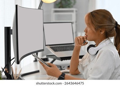 Young female programmer analyzes code on a dual monitor setup in a modern workspace.
