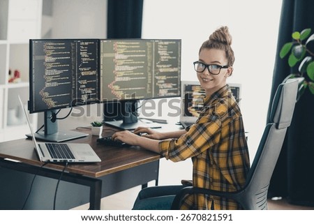Young female programmer coding software at workspace with multiple screens showcasing dynamic coding environments