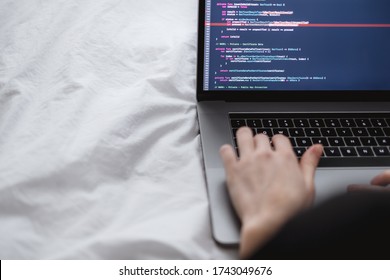 Young female programmer writes program code on a computer laptop in the bed at home. remote work