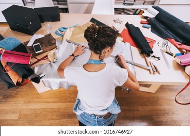 Young female purse maker working with leather textile at her workshop. Crafting tools on wooden table. Tailor, leather craftswoman wearing apron
indoors
 - Powered by Shutterstock