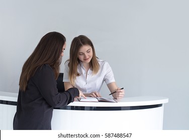 Young Female Receptionist At Medical Clinic Or Hospital Discussing Schedule With Patient And Writing Record To The Note Book . 